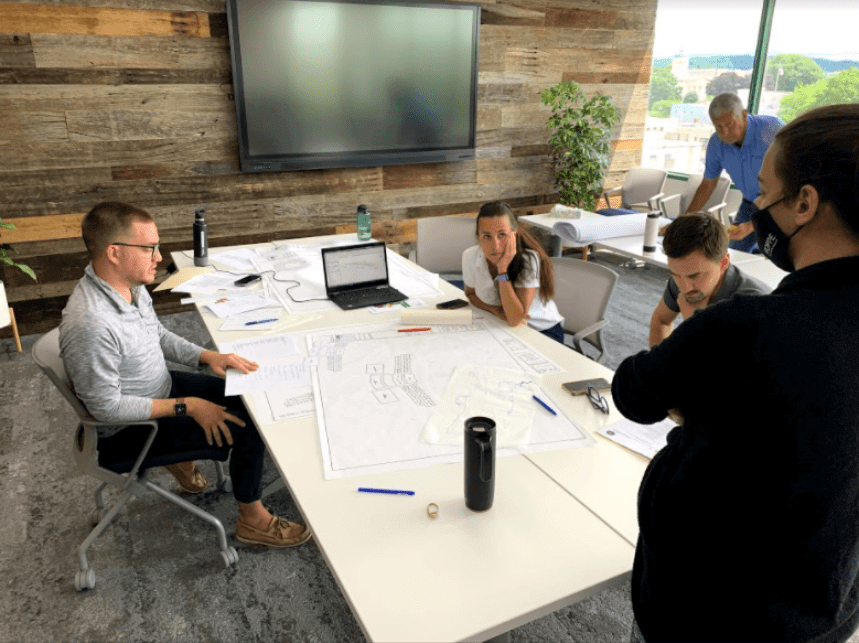 Five people in a conference room with a tv mounted on the wall, reviewing a new blueprint.