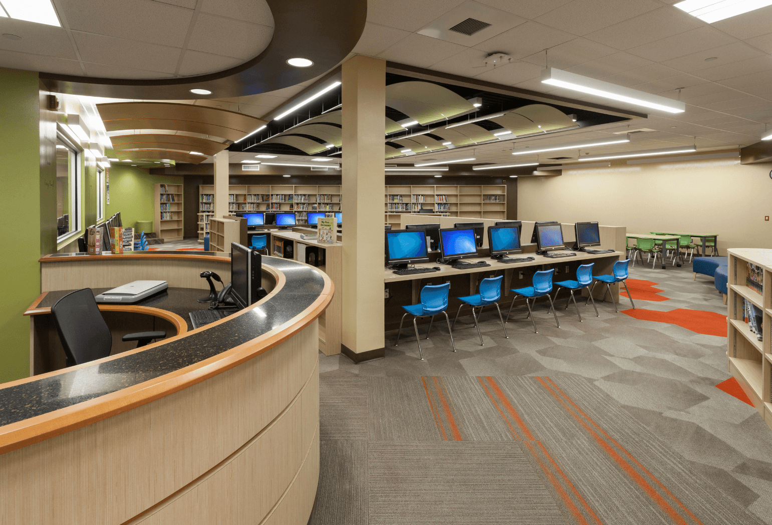 A school library with a front desk, computers, and bookshelves.
