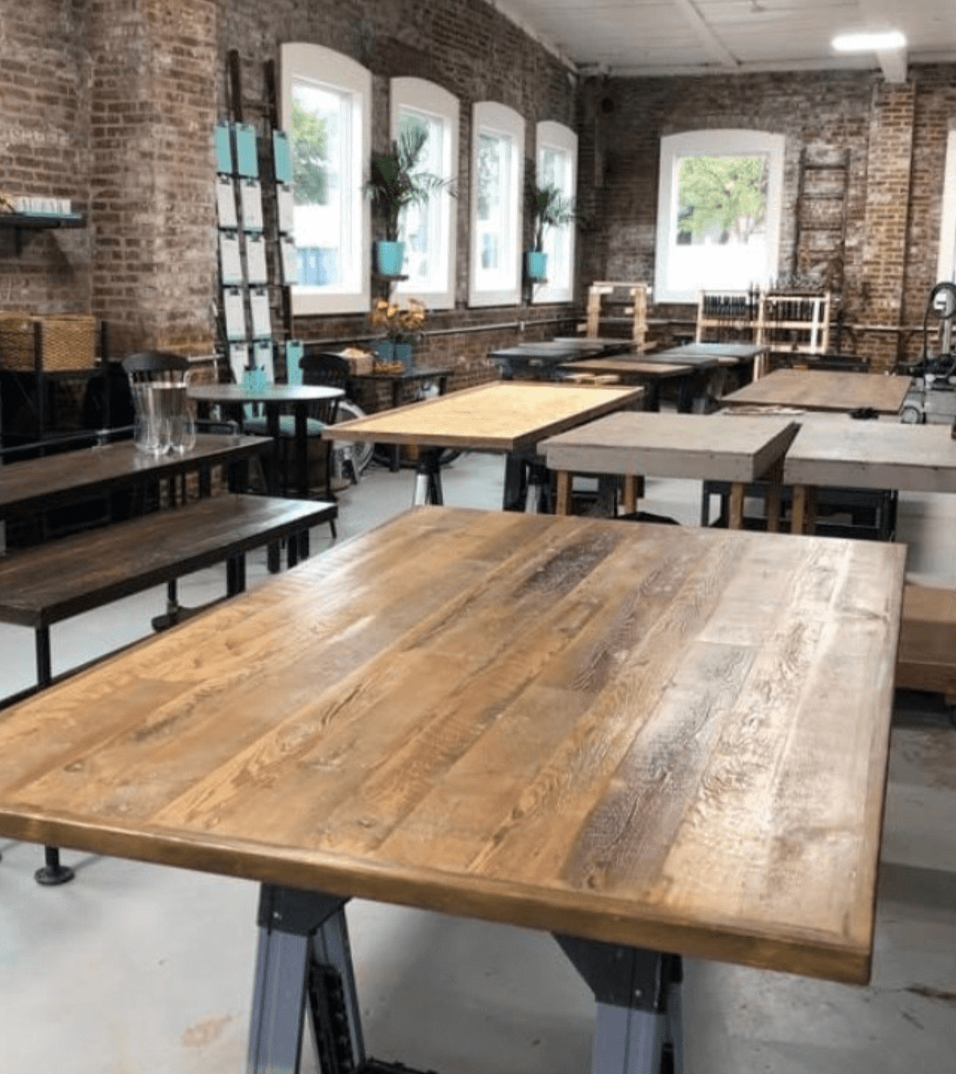 Multiple wooden tables in an exposed brick building with natural light coming through the large windows.