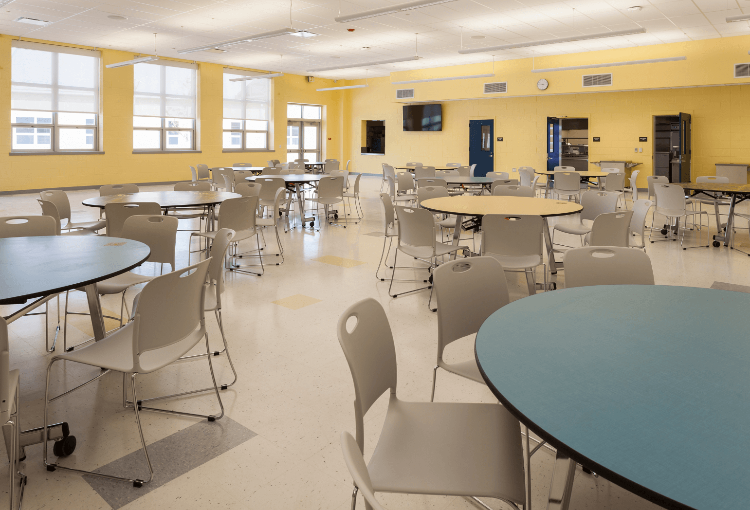 A cafeteria with yellow walls, circular tables, and beige chairs.