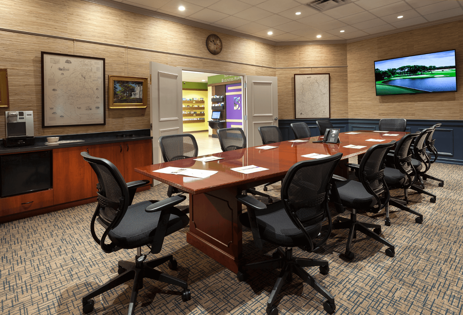 A conference room with a large table, multiple chairs, a mounted tv, and other mounted photo frames.