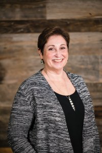 Principal & CEO of SSP Architectural Group, Jeanne Perantoni, posing for a headshot in front of a wood paneled wall. 