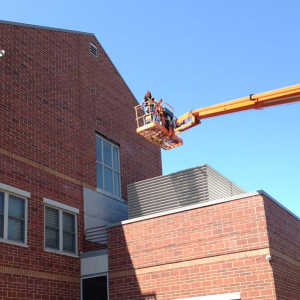 Tammy on a boom lift in front of a brick building.